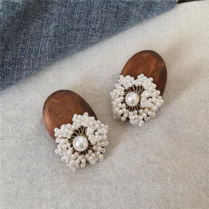 Detail view of ethnic style wood and pearl floral stud earrings on textured fabric