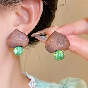 Close-up of ethno-style heart-shaped wooden earrings with green marbled bead pendants