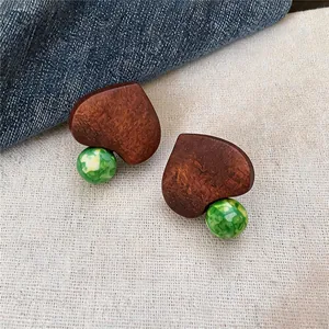 Close-up detail of ethnic style wooden heart-shaped earrings with green marbled glass beads