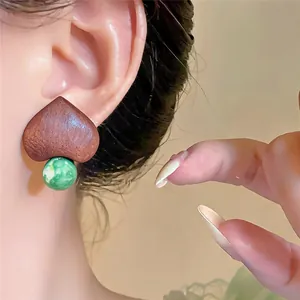 Detailed macro view of heart-shaped wooden earring with green marble bead on a model ear