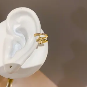 Primer plano de un ear cuff dorado de doble capa con circones en un modelo de oreja
