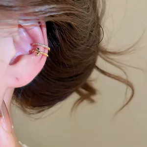Detalle de un elegante ear cuff dorado de doble capa con circonitas y un motivo de hoja pequeña.