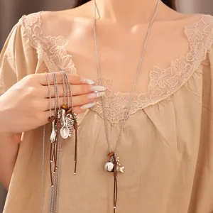 Detail shot of long sweater necklace with silver comb and fish charms on a brown leather cord.
