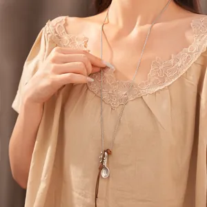 Detailed view of long sweater necklace featuring spoon and fish charms on model