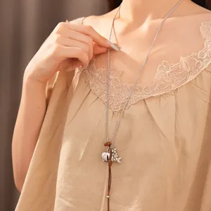 Close-up of long sweater chain with fish and comb charms on a beige top