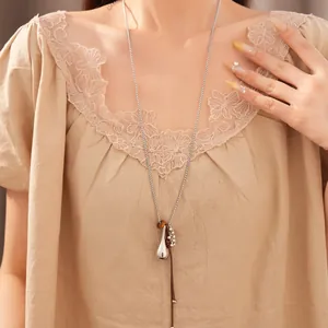 Detail shot of long necklace with silver-tone pendant and brown leather cord on model.