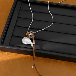 Close-up view of a silver fish pendant necklace with a leather cord on a black tray.