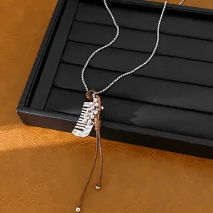Detailed view of a silver comb pendant and brown leather cord on a sweater necklace