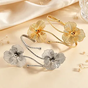 Detailed view of elegant golden and silver hollow flower arm cuffs on a silk background