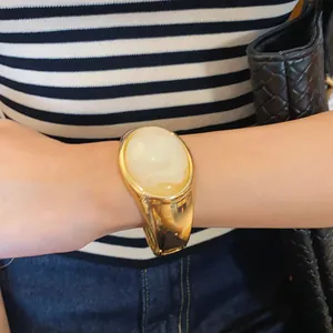 Close-up of a wide gold cuff bracelet with a large oval cream stone inlay on a wrist.