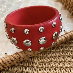 Close-up of a red wooden bangle with polished silver-tone rivets on woven texture.