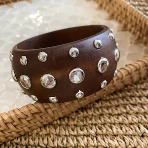 Detailed view of a wide dark brown wooden bangle embellished with shiny silver rivet studs.