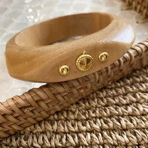 Macro view of geometric wooden bangle featuring gold rivet studs and woven texture