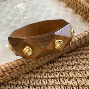 Close-up of geometric wooden bangle with gold rivets and natural wood grain texture