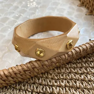 Detailed view of an irregular geometric wooden bangle featuring gold studs on a woven surface.