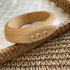 Detail view of a natural wooden bangle with three gold-tone metallic stud accents.