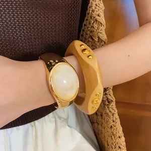 Detailed view of irregular wooden rivet bangle and gold cuff with oval white stone