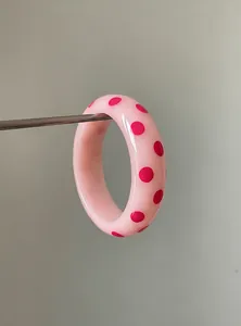 Detailed macro shot showing the smooth resin texture and pink polka dot pattern of the bangle