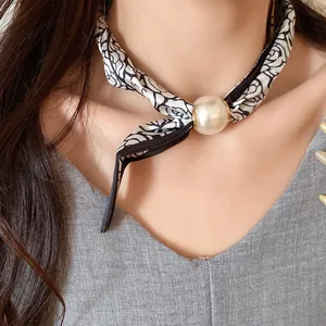 Gros plan d'un collier foulard en soie élégant avec pendentif perle et motif rose