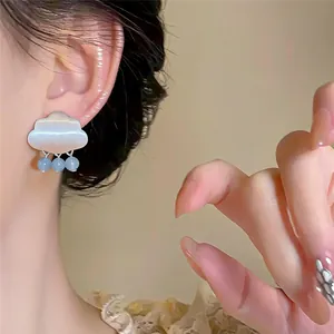 Detalle de un pendiente en forma de nube con cuentas de gotas de lluvia azules en la oreja