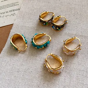 Primer plano de pendientes de aro bañados en oro de 18k con nácar y cristales incrustados.