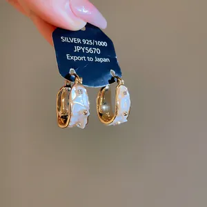 Detalle de pendientes de aro de concha dorados con diamantes