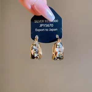 Detalle de pendientes de aro chapados en oro de 18k con nácar natural y piedras brillantes.