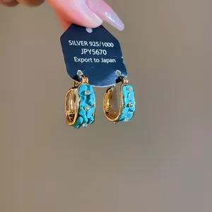 Detalle de pendientes de aro bañados en oro de 18k con piedras turquesas y pequeños cristales