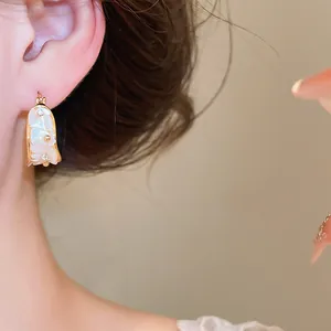 Detalle de un pendiente de aro de concha bañado en oro de 18k con brillantes diamantes