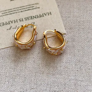 Vista macro detallada de pendientes de aro bañados en oro de 18k con nácar y cristal