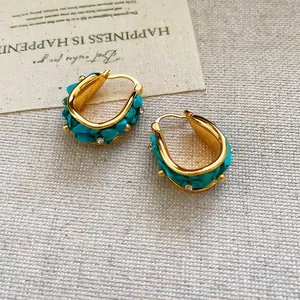 Primer plano de pendientes de aro bohemios bañados en oro 18k con turquesa y cristales.