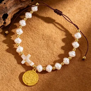 Close-up of handmade woven bracelet with baroque pearls, white cross and gold medal