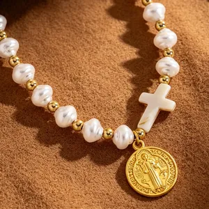 Macro detail of natural pearl bracelet featuring a white cross and gold religious medal