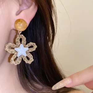 Close-up of bohemian woven straw flower earrings with white star detail for vacation