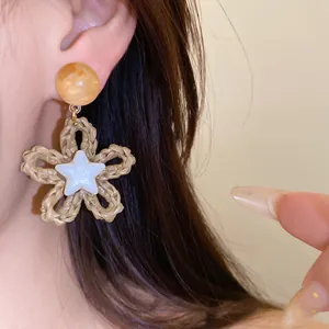 Close-up of woven paper rope flower earring with white star detail and amber bead.