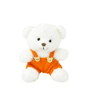 Simpatico orsetto di peluche bianco che indossa una salopette di velluto a coste arancione