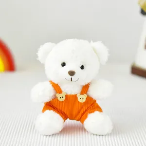 Piccolo orsetto di peluche bianco con salopette di velluto a coste arancione