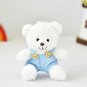 Primo piano di un orsetto di peluche bianco con salopette di velluto blu e bottoni