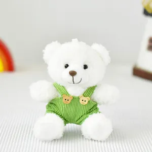 Dettaglio di un morbido orsetto di peluche bianco con una simpatica salopette in velluto verde.