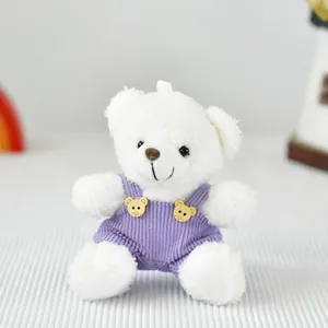 Primo piano dettagliato di un orsetto di peluche bianco con salopette in velluto a coste viola.