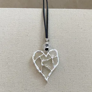 Primo piano di un ciondolo a cuore geometrico traforato in argento con cordino