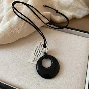 Dettaglio di una collana con ciondolo nero circolare in legno e sfera d'argento