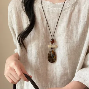 Dettaglio di una collana etnica con pendente in pietra occhio di tigre su camicia di lino