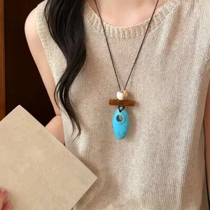 Collana etnica retrò con pendente in legno e ovale turchese su top in maglia beige.