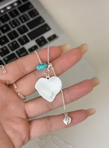 Gedetailleerde opname van witte hars hart hanger ketting met een blauwe turquoise kraal erop.