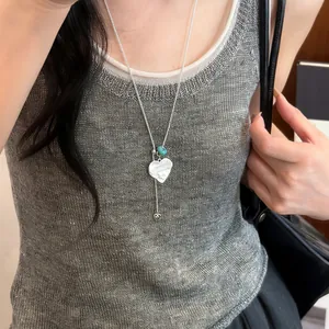 Detailopname van een zilveren hartjesketting met blauwe kraal gedragen door een model