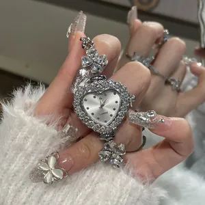 Macro view of a heart-shaped rhinestone watch with flower charms on a silver bracelet.
