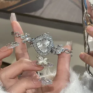 Close-up of heart-shaped rhinestone watch with flower bracelet held by manicured hand
