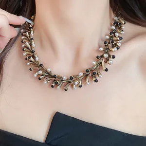 Vintage gold geometric necklace featuring white pearls and black beads worn by a model