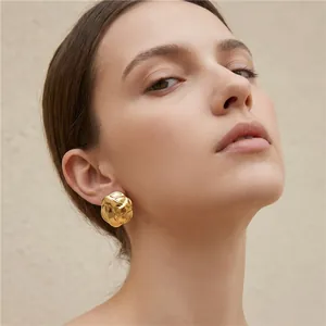 Detailed close-up shot of a textured gold-tone geometric irregular stud earring worn by a model